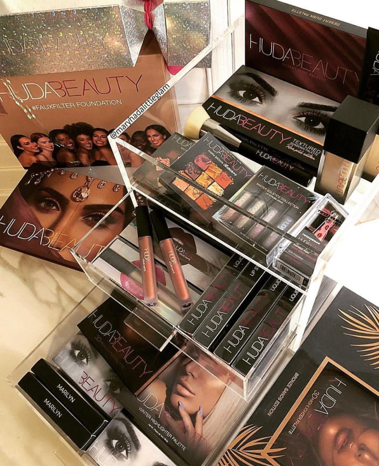 An acrylic makeup organizer filled with Huda Beauty Products.